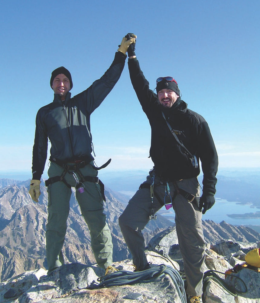 two brothers joining hands standing on top of the grand teton mountains